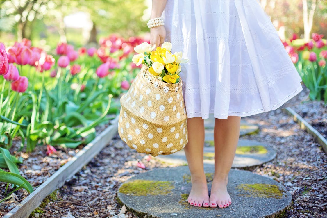Woman, shown only below the waist, holding flowers in a garden