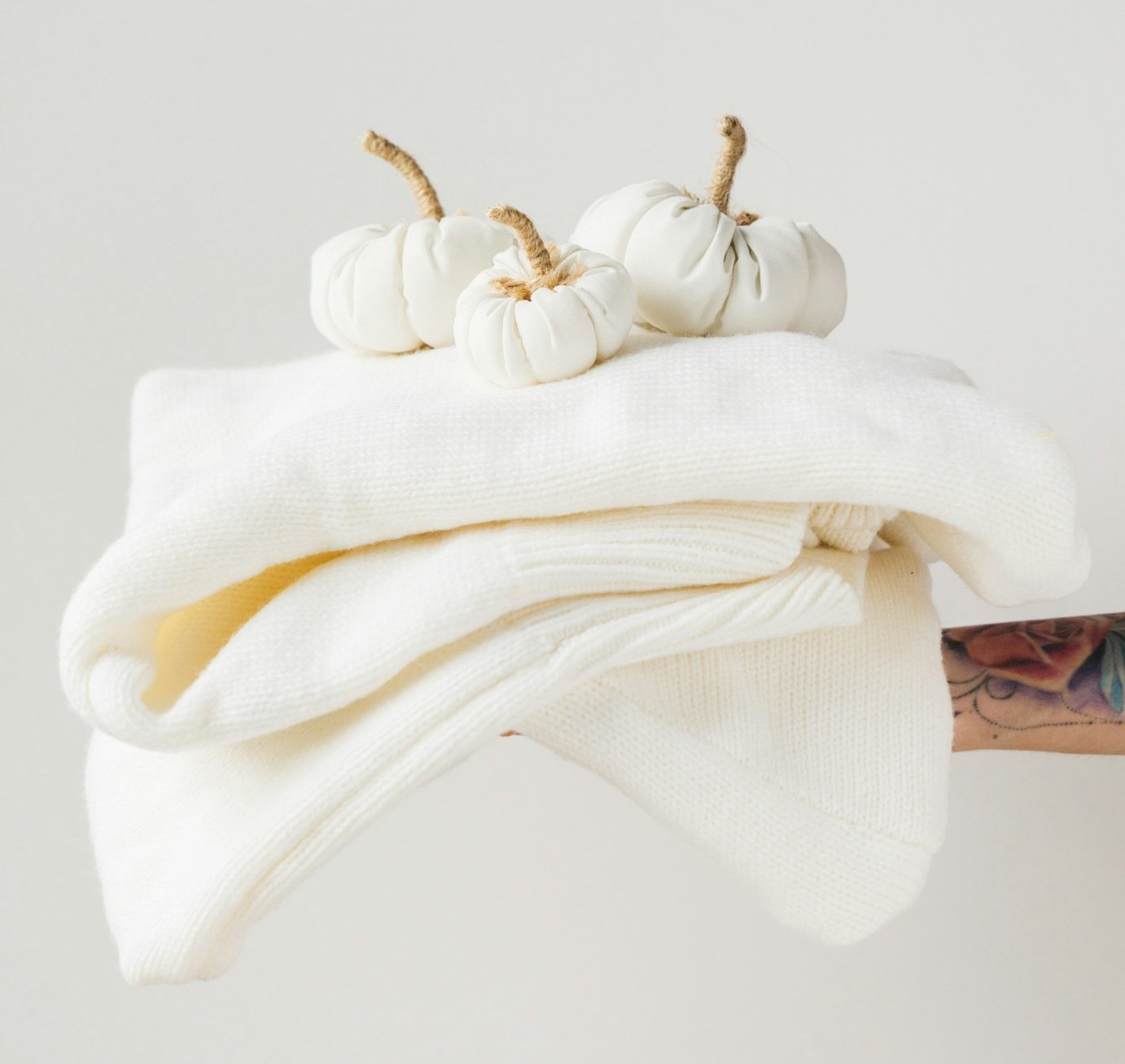 A folded cashmere sweater with white pumpkins on top.