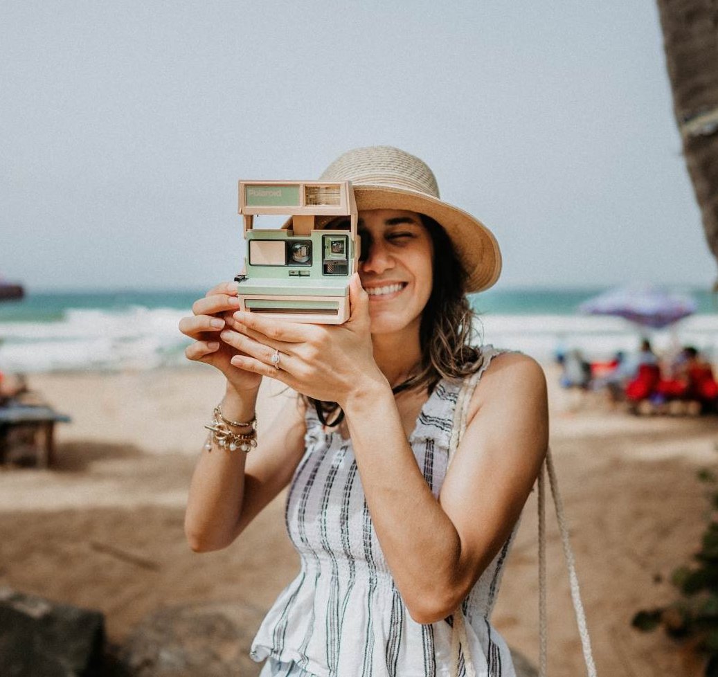  Woman holding a camera in travel attire on a beach vacation