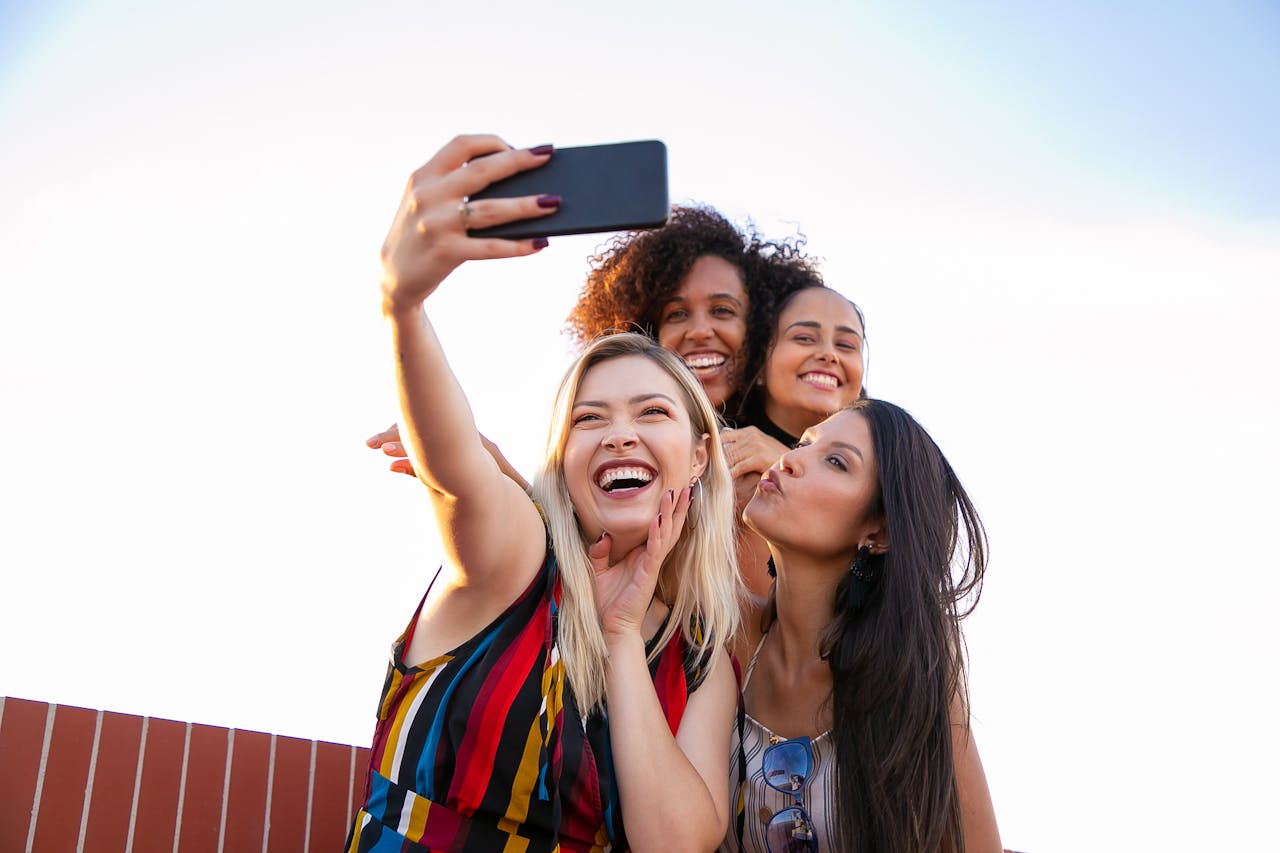 Four women taking a group selfie wearing spring vacation outfits.