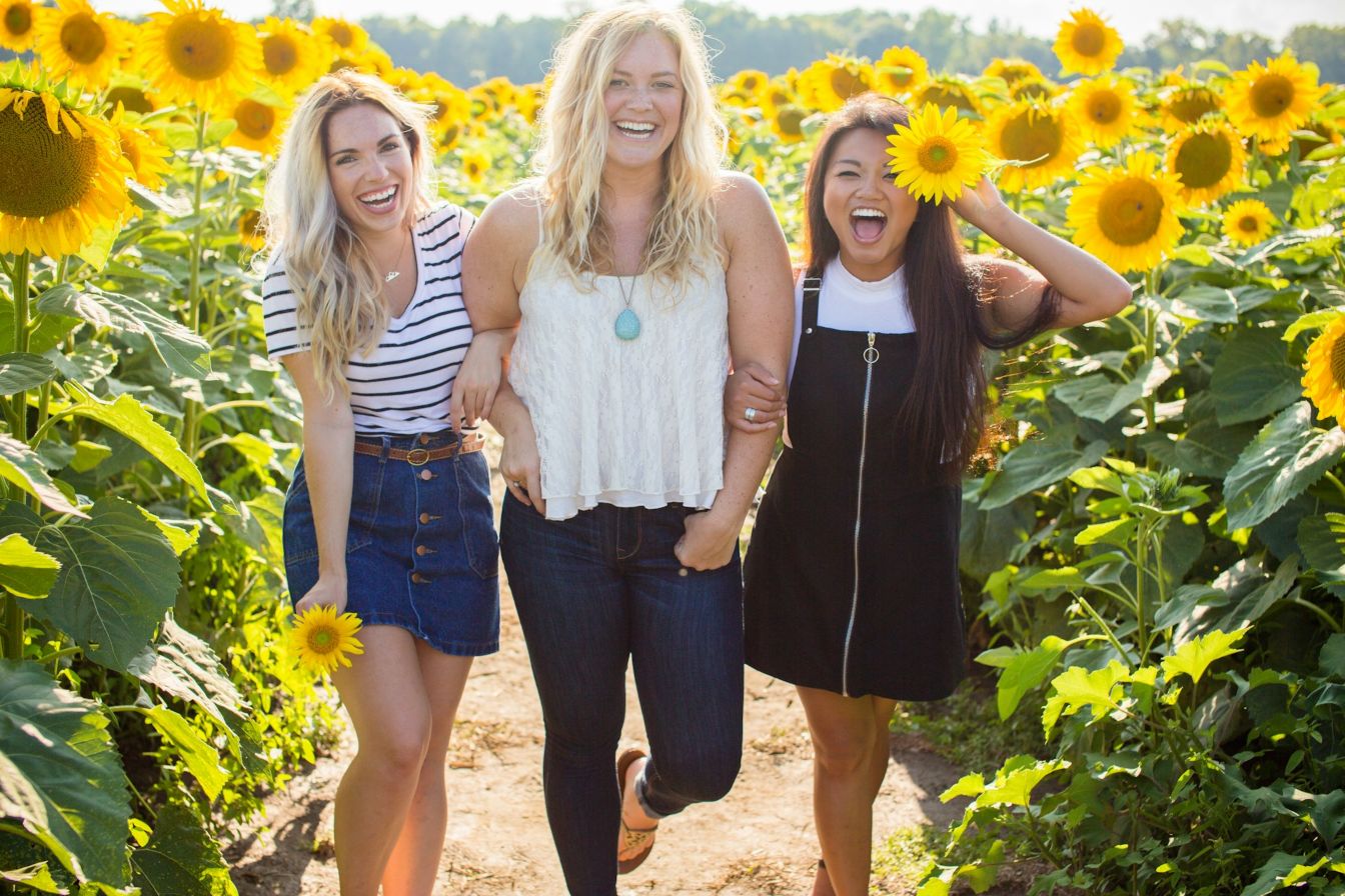 Three women in a sunflower garden wearing summer travel outfits