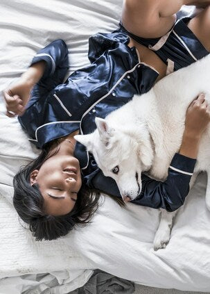 Woman wearing clearance pajamas and lying in bed next to a husky 